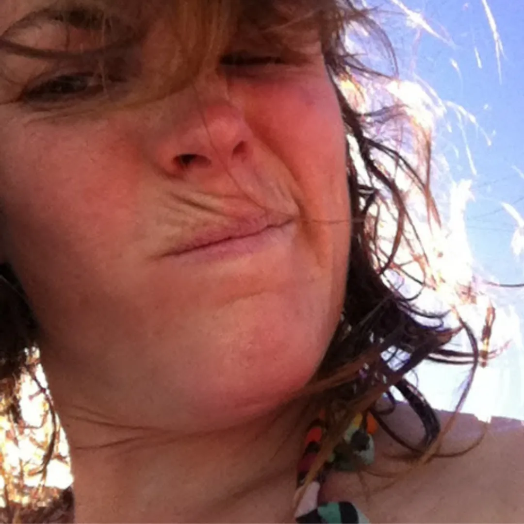 A woman squinting into the sun with her hair blowing in the wind