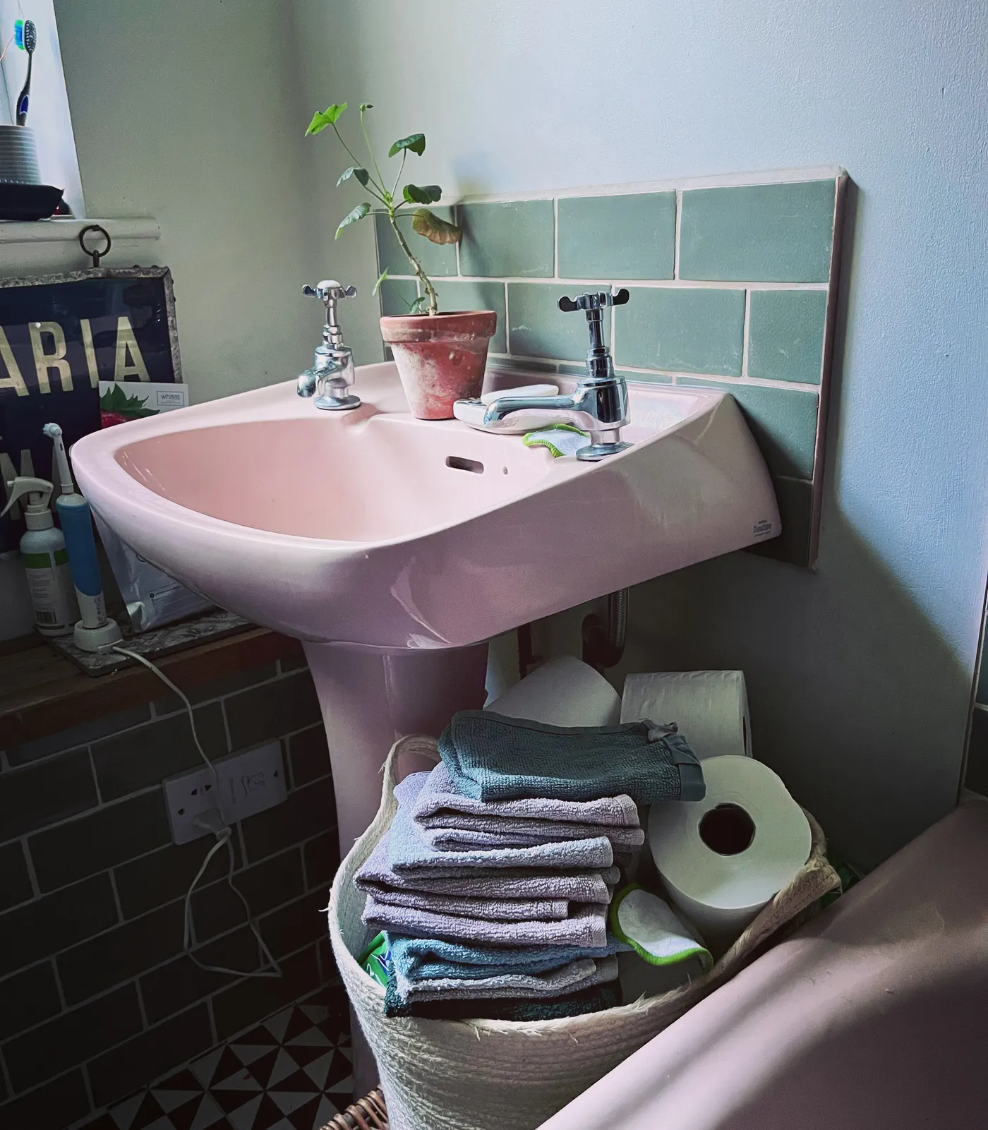 A small pink bathroom sink with folded flannels and a plant