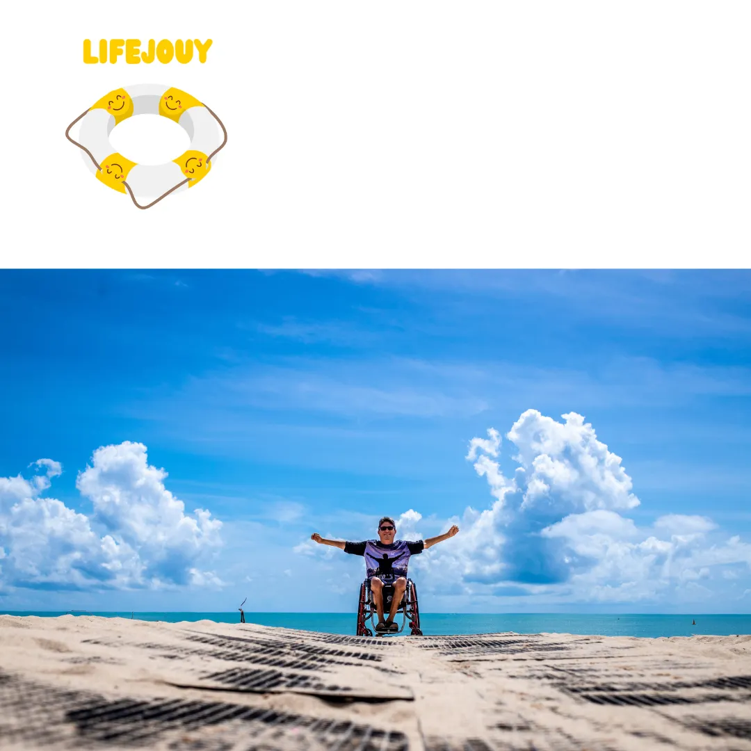 A man in a wheelchair on a sandy beach with his arms outstretched under a blue sky